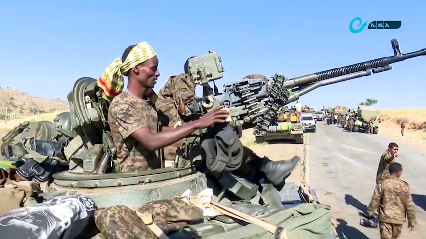 On a bright day, you view a soldier in a gun turret on a tank on a desert road.