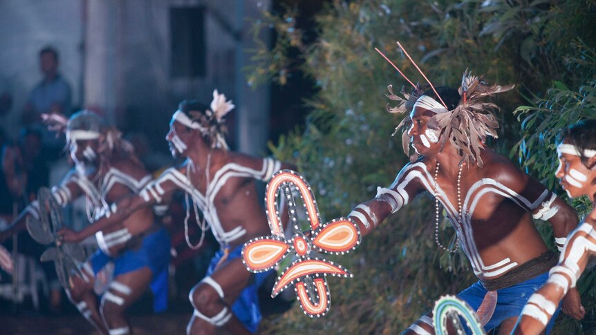 Indigenous dancers perform wearing traditional body paint and costumes, including headdresses made of feathers and gum leaves.