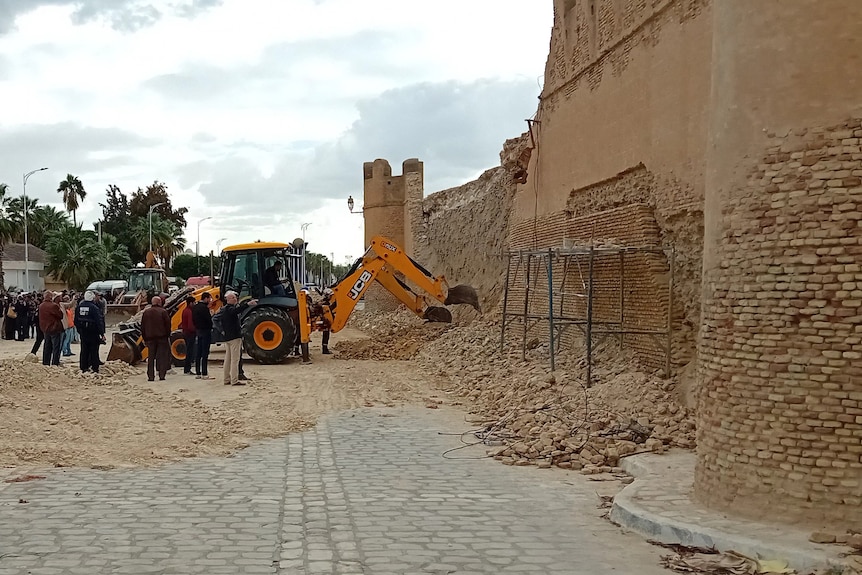 Excavators scraping rocks away from a beige old wall