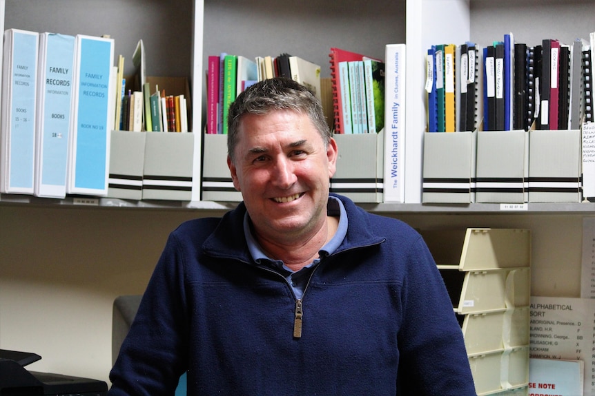 A man stands in front of a shelf filled with folders. 