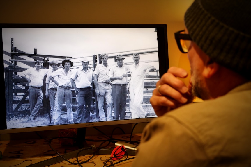A man looks at a black and white photo of a group of men standing together.