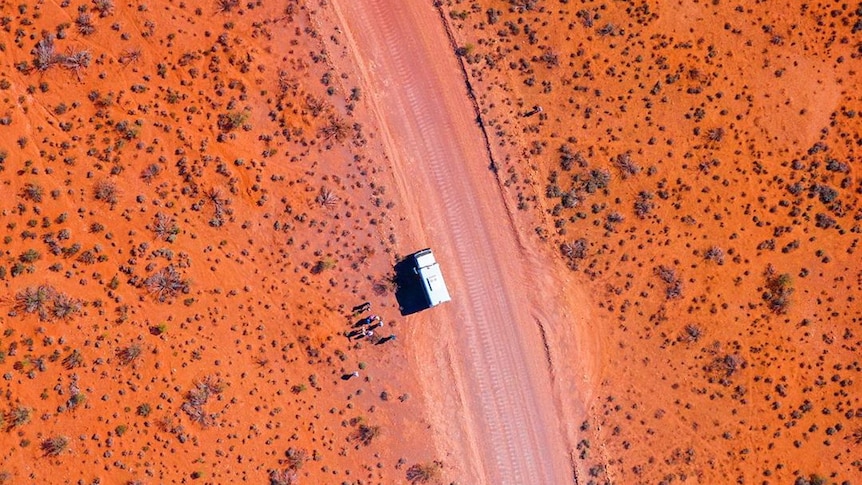 A drone photo of a car parked on the side of the road running through the red dirt of a desert.