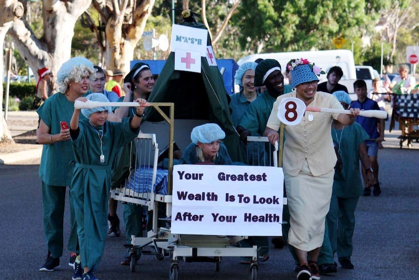 A group of people dressed in surgical green robes push a hospital bed along the street in Moora.