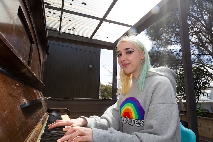 Bridie Fahey smiles as she sits at the piano and plays, dressed in a grey jumper with a bright rainbow design.