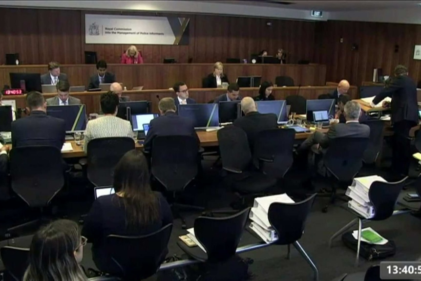 A series of courtroom beaches occupied by lawyers and a commissioner in red by herself on the top bench.