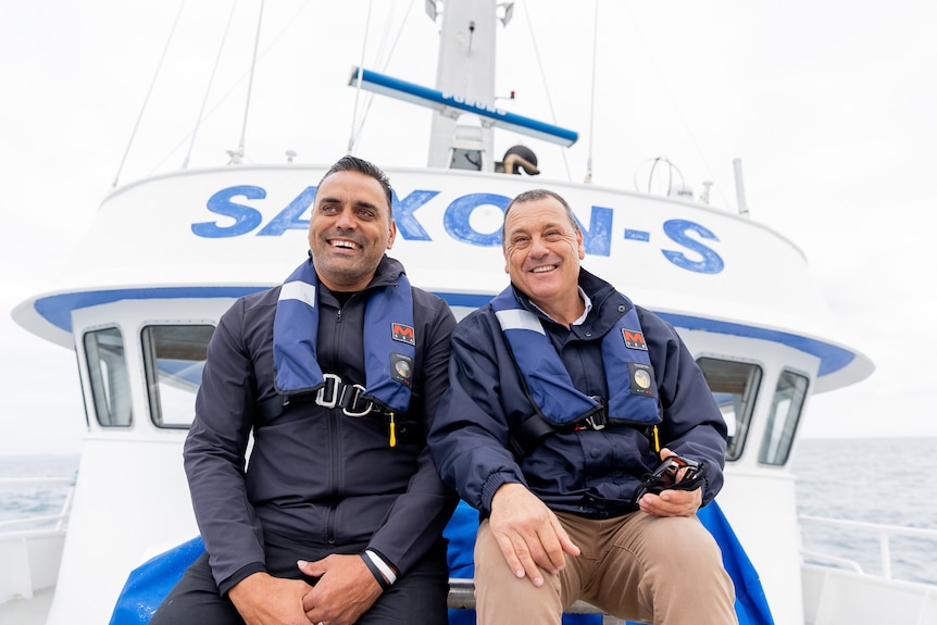 Two men sit at the front of a tuna boat both wearing life jackets