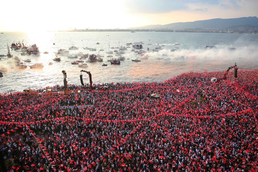 A massive crowd of supporters holding Turkish flags gather near the bay.