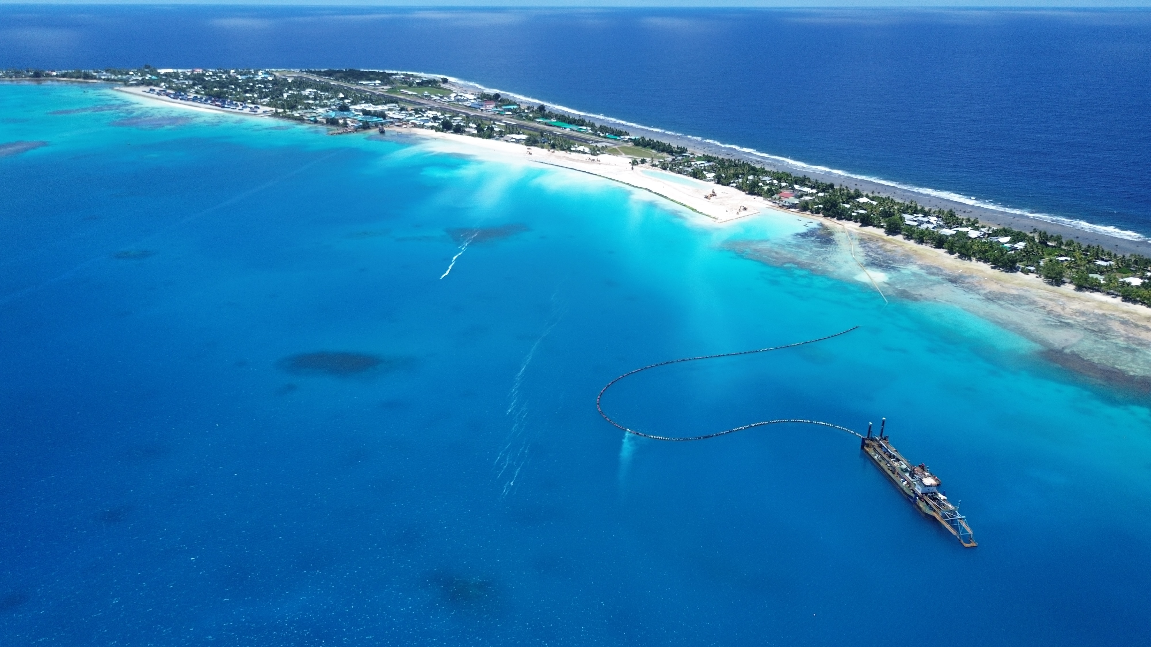 This aerial shot of a land reclamation project shows a suction dredge at sea, with excavators and the airport in the distance.