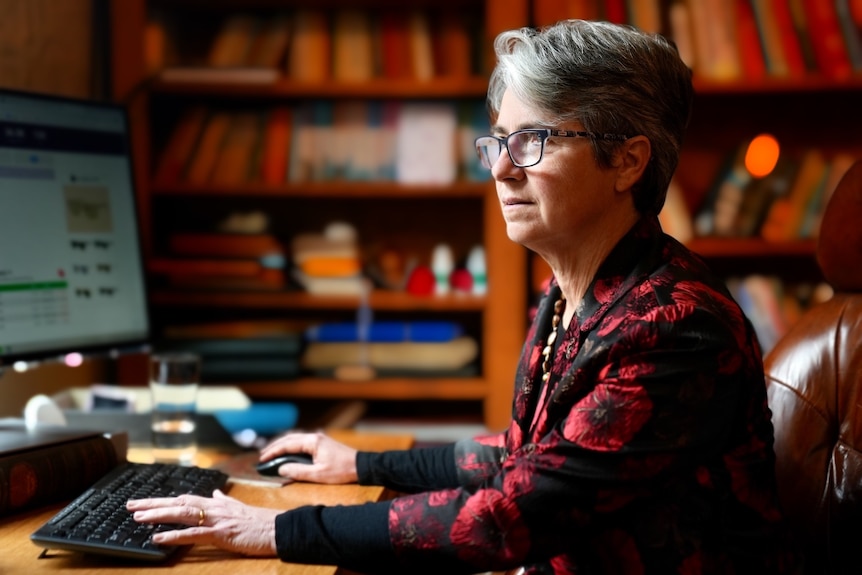 A middle-aged woman sits at her desk working on her computer 