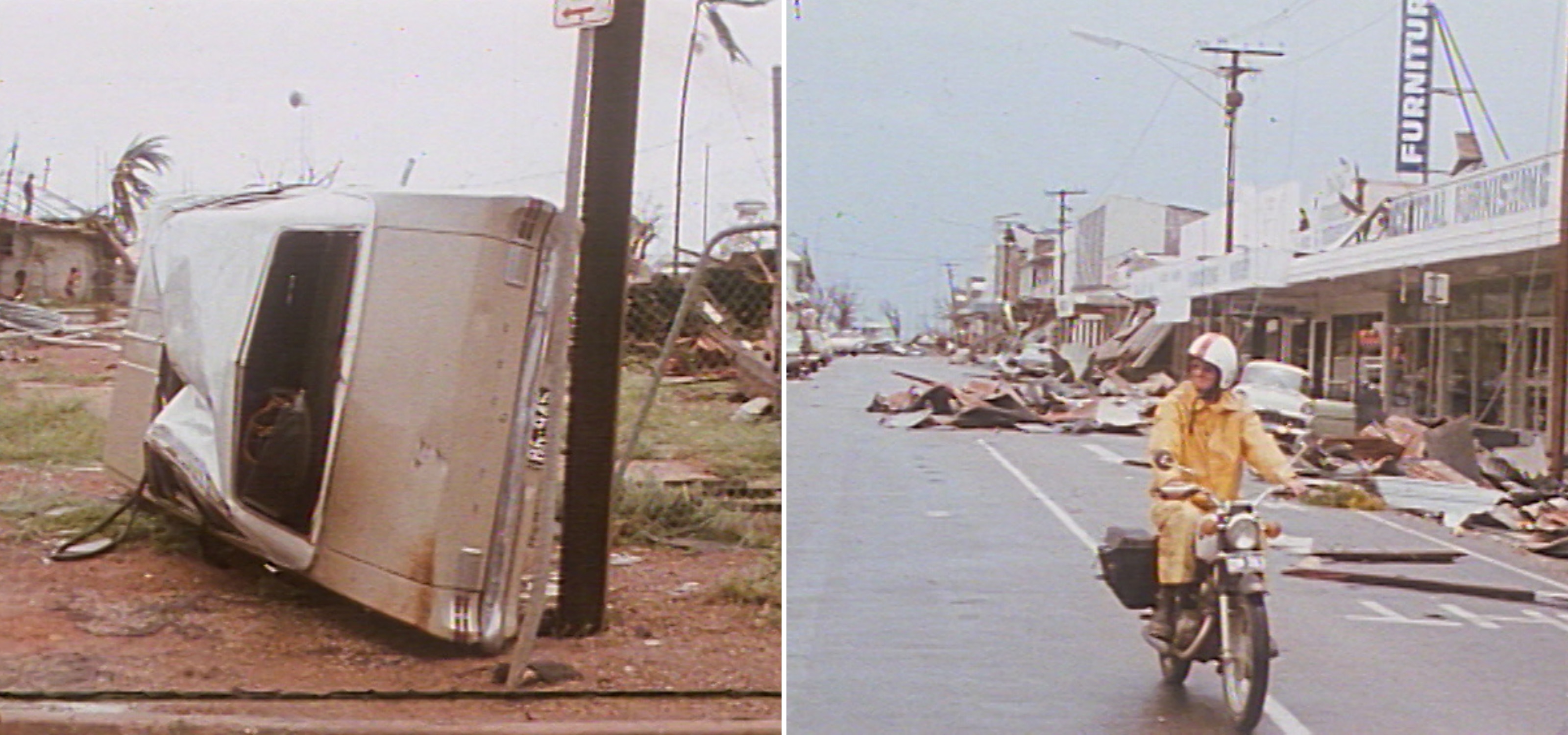 1970s sedan lies on its side next to a power pole. Man on a posty bike rides down street strewn with debris