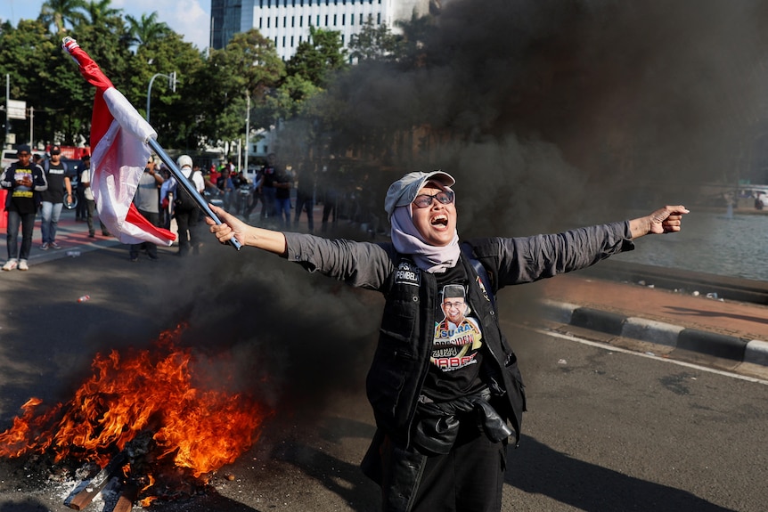 A protester shouts as she raises an Indonesian flag as tyres are burned during a protest.