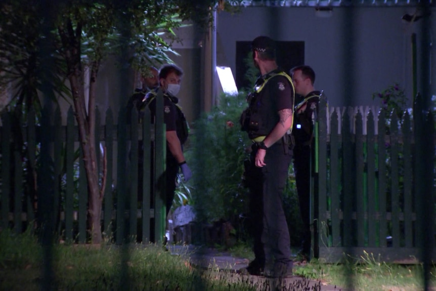 Three officers can be seen through a fence, masked, outside a residential building.