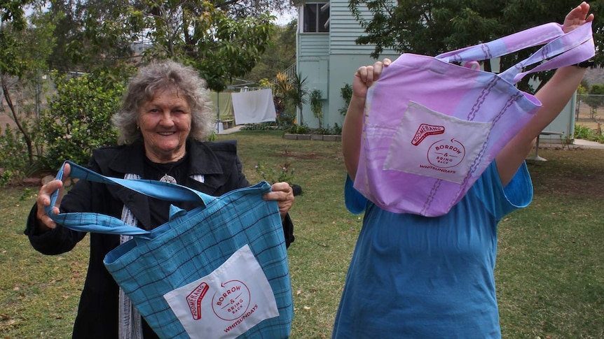 Two women hold up reusable fabric bags joyously.