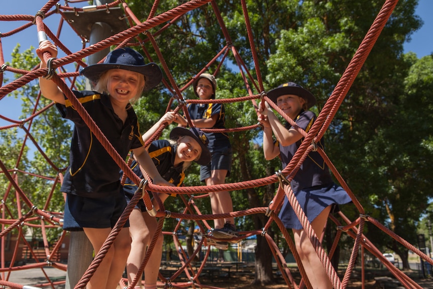 Children looking at camera smiling, on play equipment.