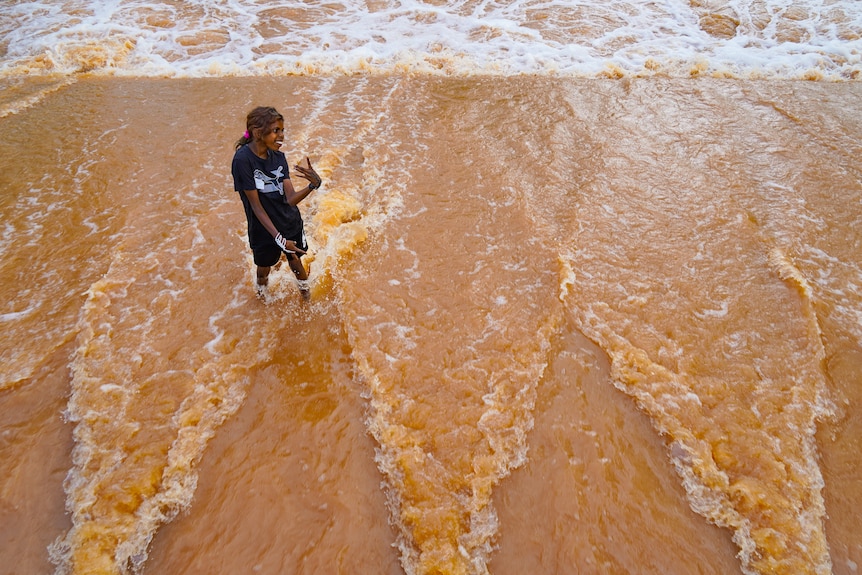 an aboriginal girl standing in floodwater smiling