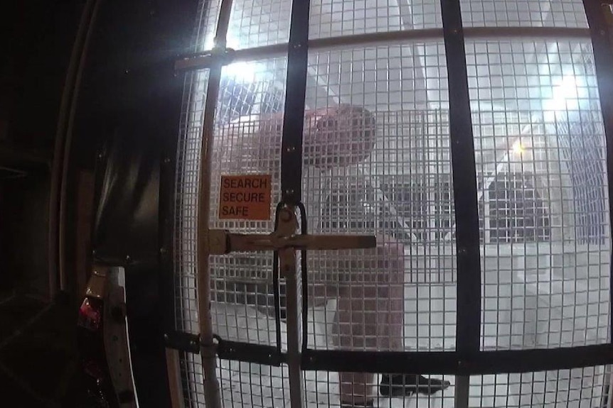 Benjamin Hoffmann sits in the back of a police cage in a police car after his arrest.