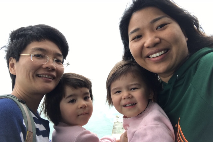 A family of two mums and two young daughters smile for the camera