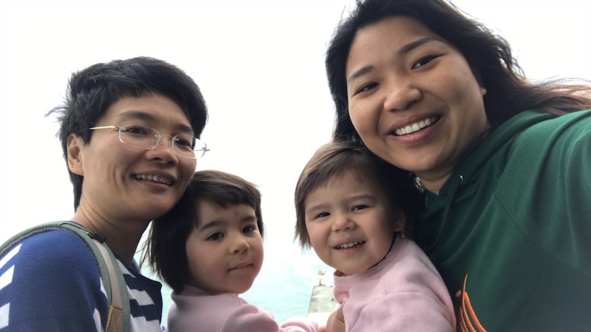 A family of two mums and two young daughters smile for the camera