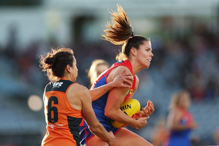 A Melbourne AFLW player tries to gather the ball for a mark as a defender attempts to stop her.