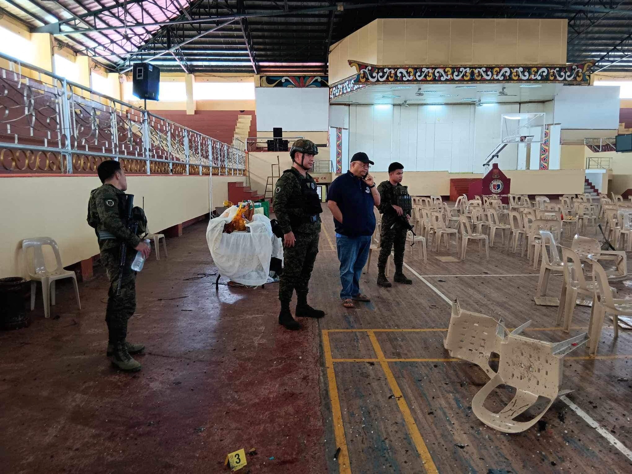 Police stand in a gymnasium covered in light debris 