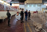 Police stand in a gymnasium covered in light debris 