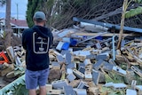 A man stands looking at a pile of rubble and bricks that has crashed down