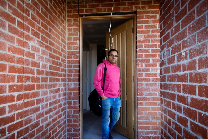 Sarthak Kanwar stands in the doorway of an unfinished brick home.