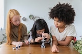 A child looks into a microscope, while two other children watch