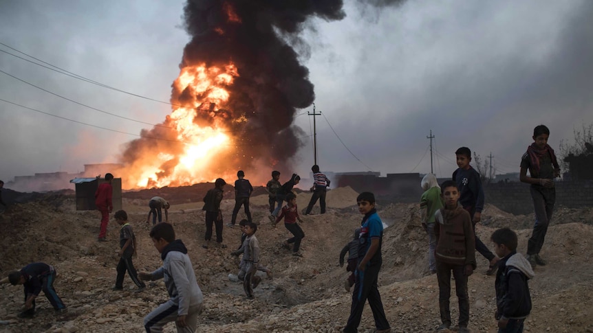 Children play next to a burning oil field in Al Qayyara, south of Mosul