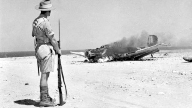 Old photo of soldier standing beside crashed fighter plane in flames