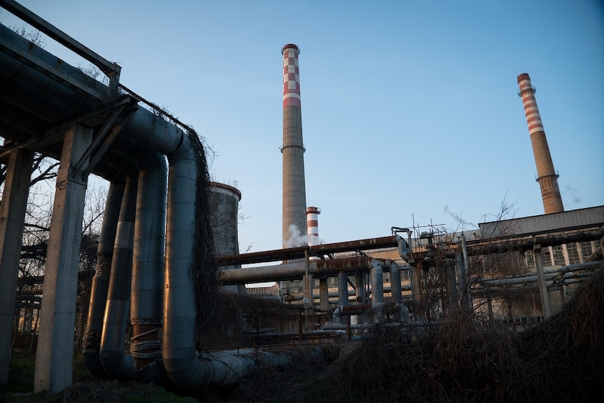 A dilapidated industrial building with two exhaust towers and large rusting pipes running into it.