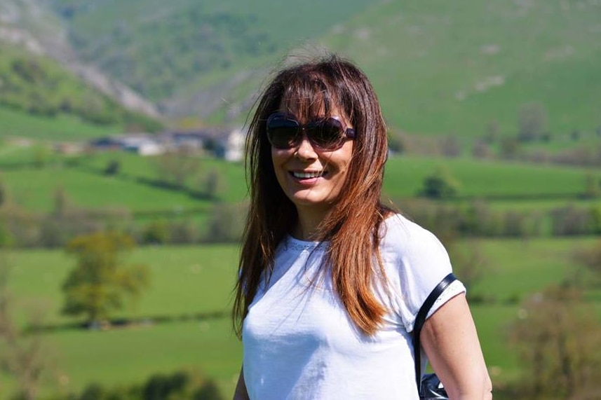 A woman with medium-length brown hair stands in front of mountains