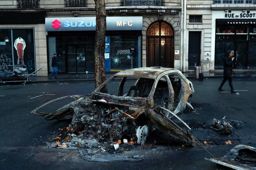 A charred car sits on a Parisian street in front of shops in the capital.