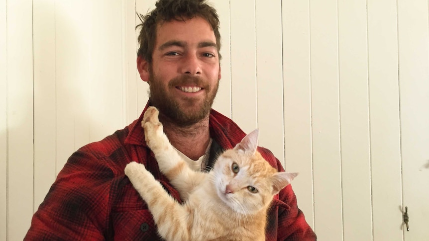 A man with a beard cuddles his ginger cat.