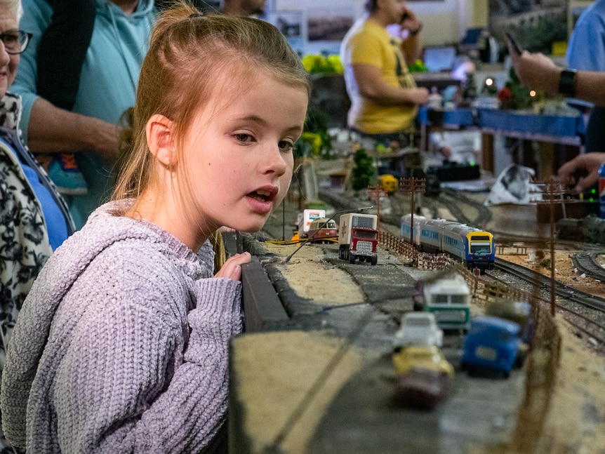 A young girl looking at miniature model railway train set.