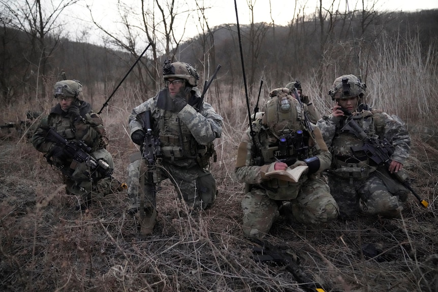 soldiers in camouflage uniforms crouch in a military drill.