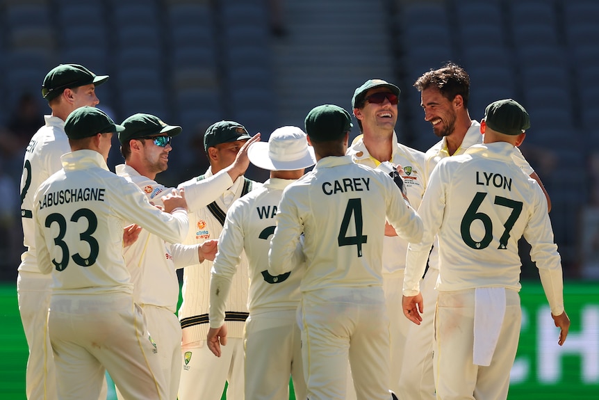 Australian Test cricket players gather on the field during a game against the West Indies to celebrate a wicket.