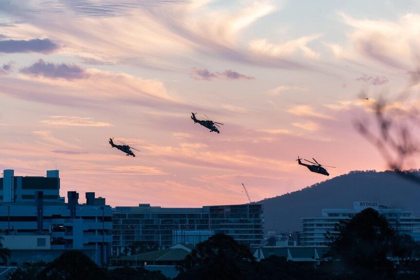 Army helicopters fly over city buildings
