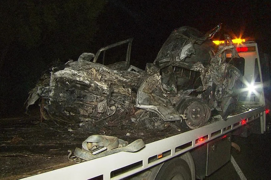 A burnt and crumpled car on the back of a white tow truck