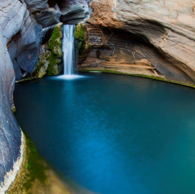 A natural pool surrounded by rock walls and a waterfall.