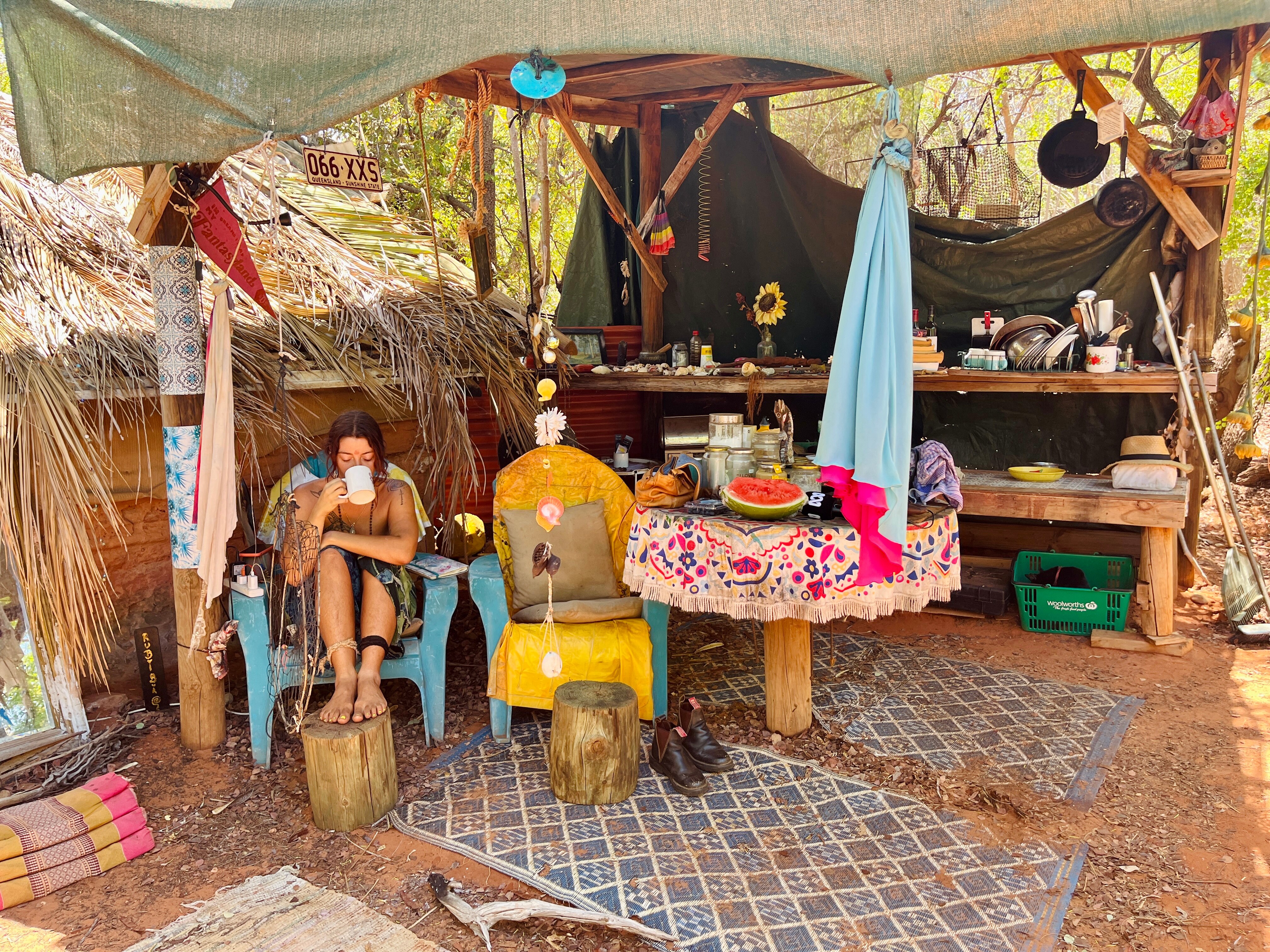 A woman sits sipping a cup of tea in an outdoor kitchen bush camp.