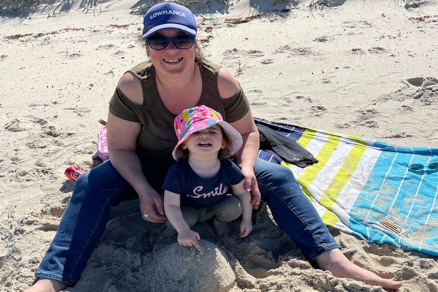 a woman and her daughter sitting on a beach