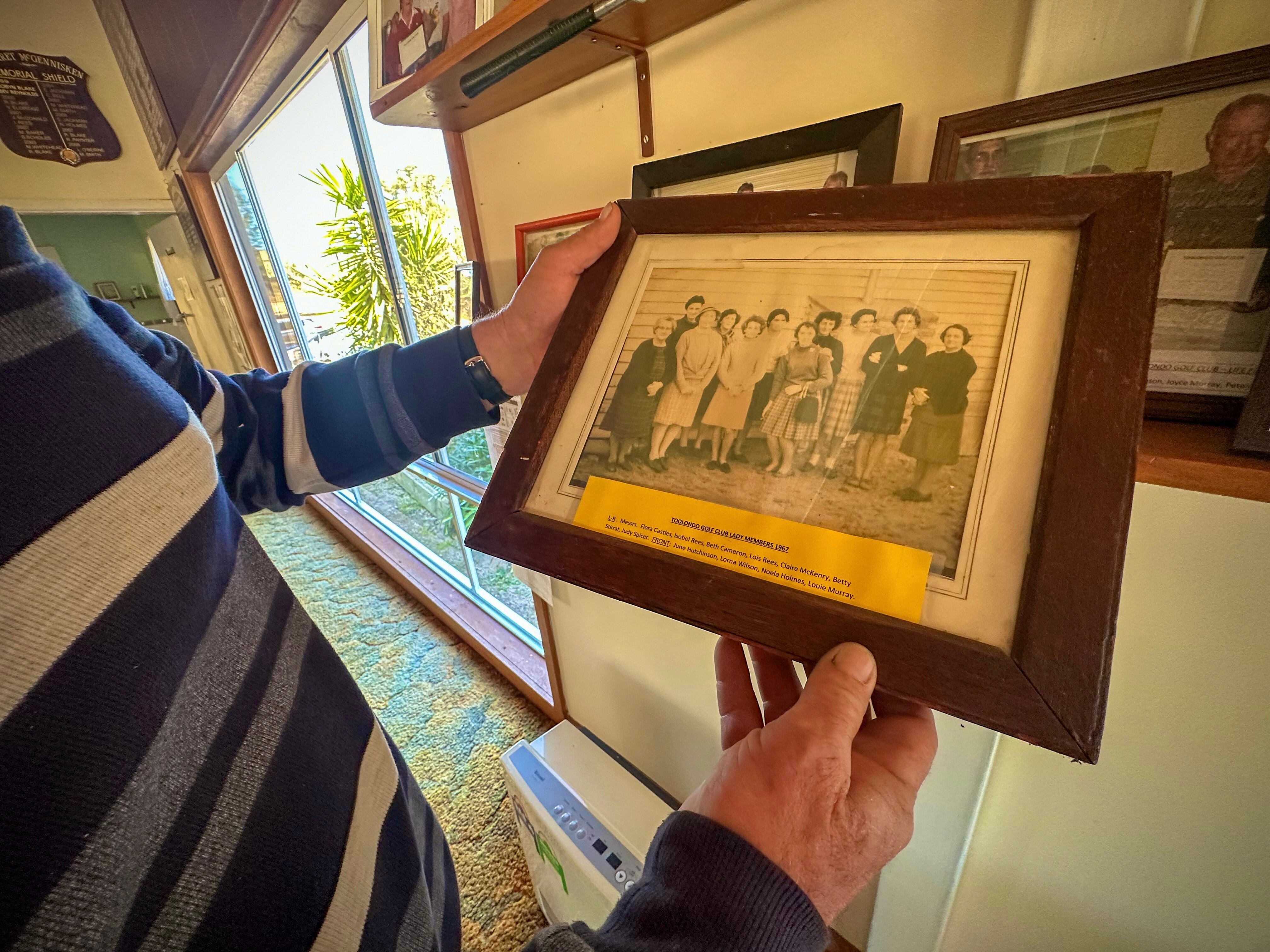 Man's hands holding a black and white framed photo of women golfers.