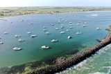 Drone shot of boats in the water with a breakwater and the shoreline in the distance.