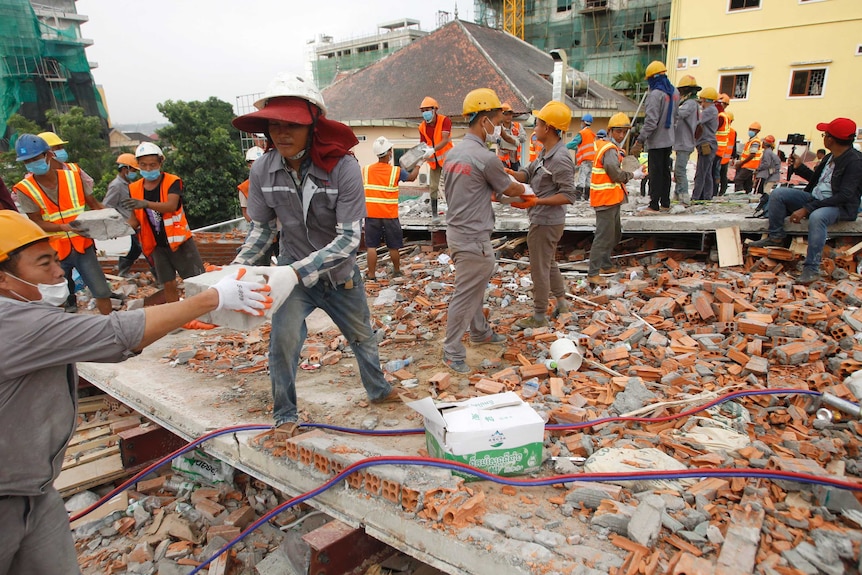 Rescue workers in grey and orange hi-vis form a line to remove the rubble of a collapsed building, brick by brick.