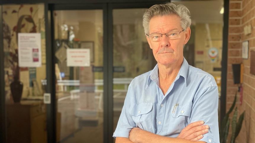 A man stands in front of a glass door with his arms crossed