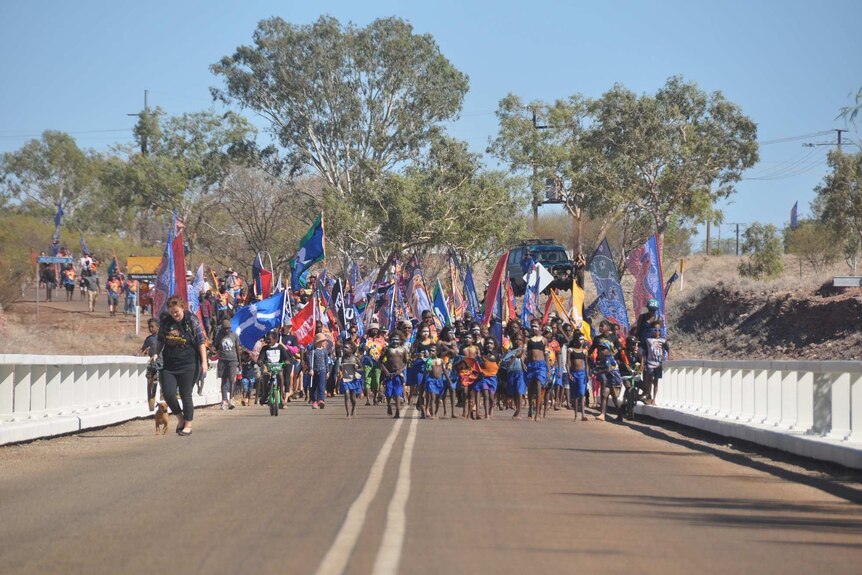 Hundreds march across a bridge with flags in Kalkarinji.