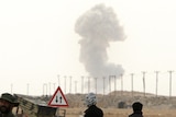 Libyan rebels taking shelter on the outskirts of Ajdabiya watch as smoke billows from near the city