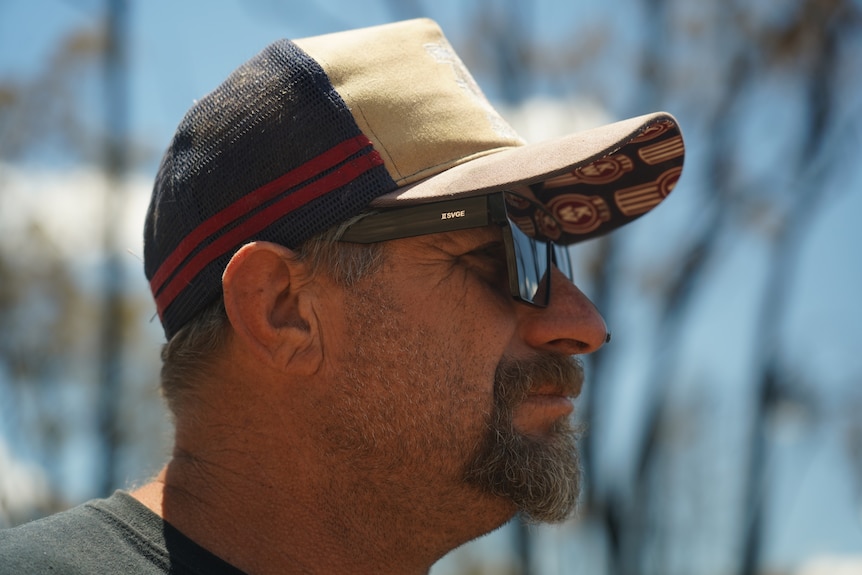 a close-up of a man looking to the right of the camera, he's wearing a cap and sunglasses