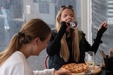Three women sit around a table drinking wine and eating pizza at a restaurant